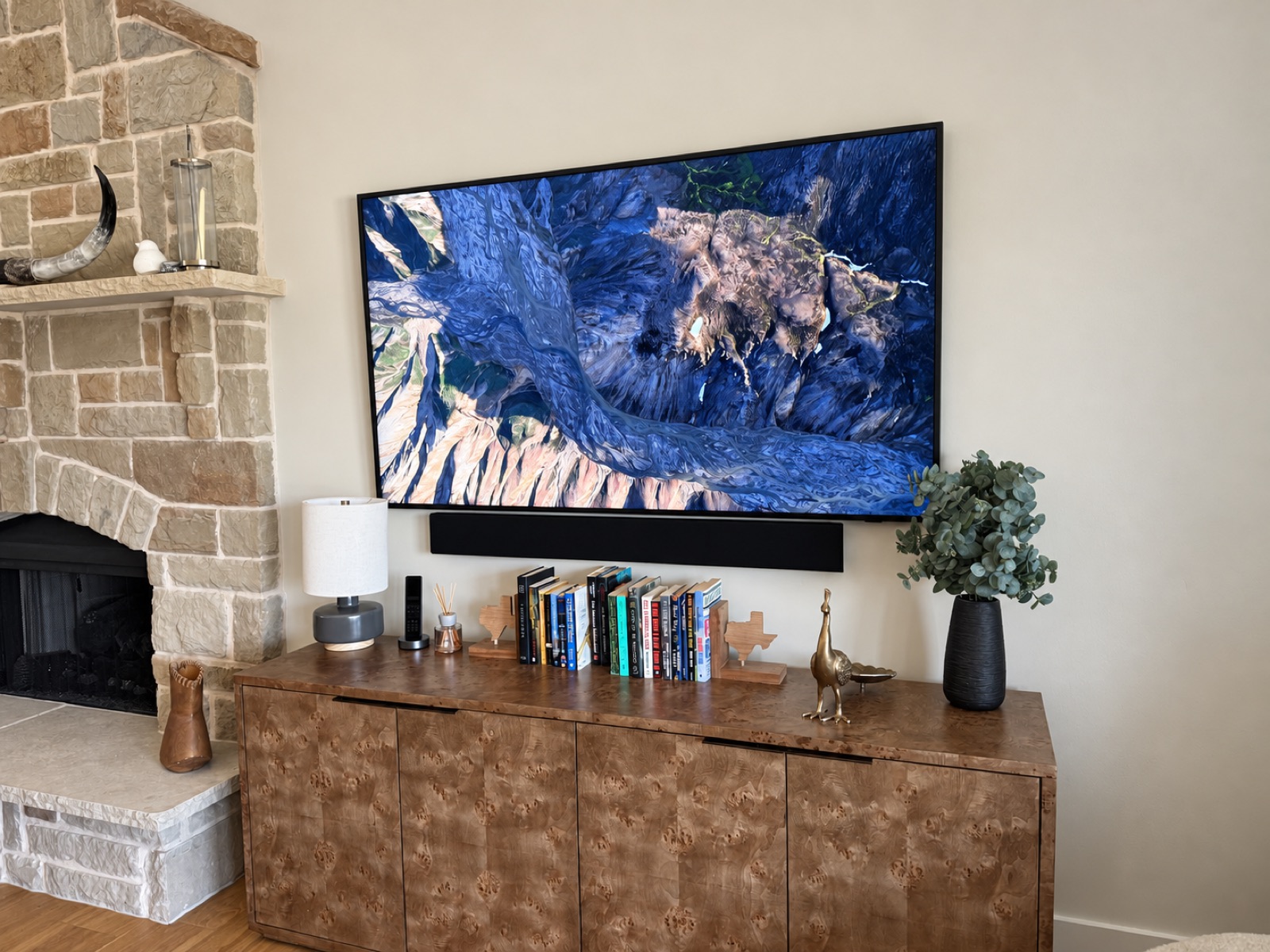 Wall-mounted TV and soundbar installed beside a stone fireplace by Eightline